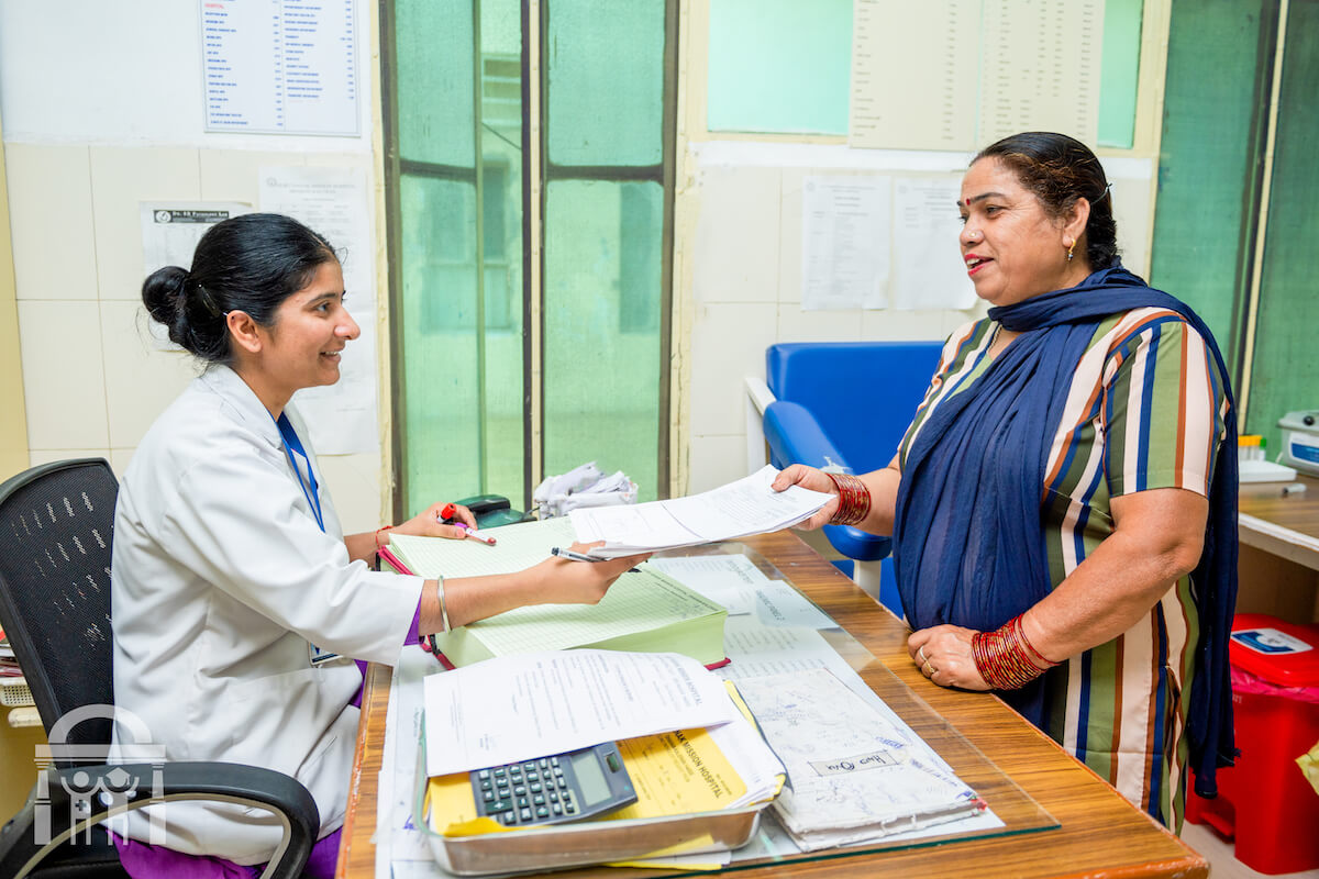 Female patient handing in paperwork at out patient clinic desk - Guru Nanak Mission Hospital medical clinic near Banga